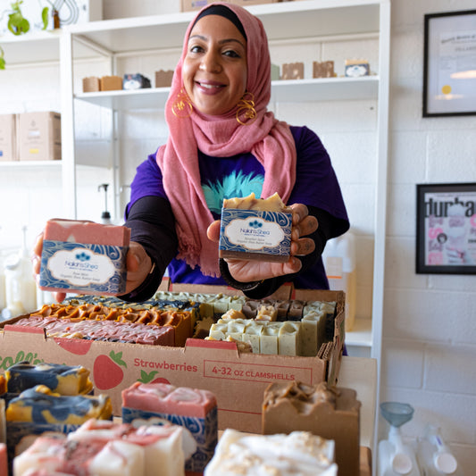 Camilia, founder of Nailah’s Shea, holding two other beautifully crafted soaps from her collection. Her hands gently cradle the soaps, showcasing their rich colors and textures, with a backdrop that highlights the artistry behind her brand.