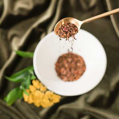 A spoonful of Ora Signature Tea Blend from Ora Tea House, showcasing the vibrant mix of South African honeybush, safflower, papaya, and cornflower blossoms. The loose-leaf tea is beautifully presented, highlighting its rich colors and aromatic ingredients.